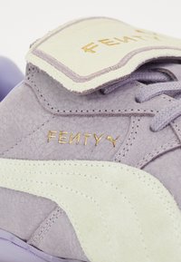 Purple leather sneaker with a suede white side stripe. Gold "FENTY" logo on the tongue. Soft texture and rounded design.