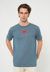 Kék, rövid ujjú pamutpóló kerek nyakkivágással. Piros "HUGO" feliratú címke középen a mellkason. Simaságú anyag és laza fazon.