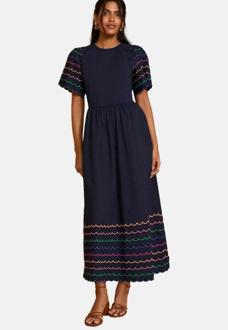 Abito lungo in cotone blu navy con maniche corte a forma di scallop e ricami colorati a motivo ondulato lungo l'orlo. Vita a sbuffo flared.