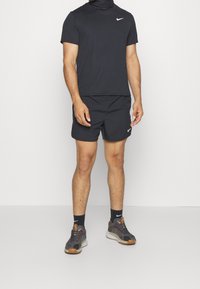 Czarny strój sportowy składający się z dopasowanej, krótkosleeve'owej koszulki i spodenek, wykonany z lekkiego materiału, w połączeniu z szarymi trampkami i czarnymi skarpetkami.