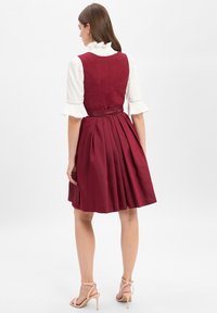 Burgundy dress with a fitted bodice, pleated skirt, and a satin waistband. White shirt with ruffled cuffs visible. Smooth fabric texture.