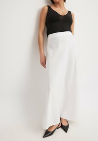 Top senza maniche nero abbinato a una gonna bianca a lunghezza caviglia realizzata in tessuto leggero. La gonna presenta una texture liscia e una silhouette svasata.
