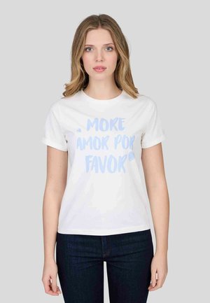 T-shirt en coton blanc avec des manches retroussées ; arbore un texte bleu clair disant "MORE AMOR POR FAVOR". Le mannequin affiche une coupe décontractée avec un jean sombre.