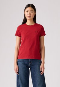 Rød bomull T-skjorte med rund hals og korte ermer. Har en liten logo på brystet. Kombinert med blå denim jeans med vid ben.
