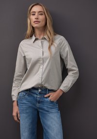 Jasnobeżowa koszula na guziki w cienkie niebieskie paski, z długimi rękawami, wykonana z miękkiego materiału. Połączona ze średnio wypranymi dżinsami o luźnym kroju.