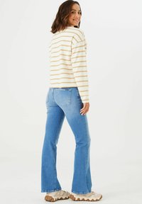 Helles und beige gestreiftes Langarmshirt kombiniert mit hellblauen Schlagjeans und beigen Sneakers, von hinten gesehen, welches die Passform des Outfits hervorhebt.