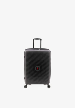 Valise rigide noire avec des lignes texturées diagonales, quatre roues pivotantes, une poignée télescopique et un petit logo carré rouge au centre.