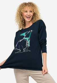 Granatowa koszula z długim rękawem z miękkiego materiału, z minimalistyczną grafiką psa i osoby w białych i turkusowych akcentach. Okrągły dekolt.