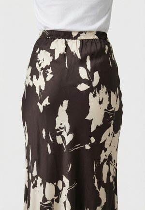 Primer plano de una falda negra de cintura alta con grandes patrones florales blancos, combinada con una blusa blanca metida por dentro.