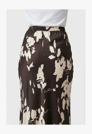 Primo piano di una gonna nera a vita alta con grandi motivi floreali bianchi, indossata con una maglietta bianca infilata dentro.