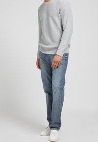 Pull en tricot gris clair avec un col rond, associé à un jean en denim bleu clair et des baskets blanches, mettant en avant un look décontracté.