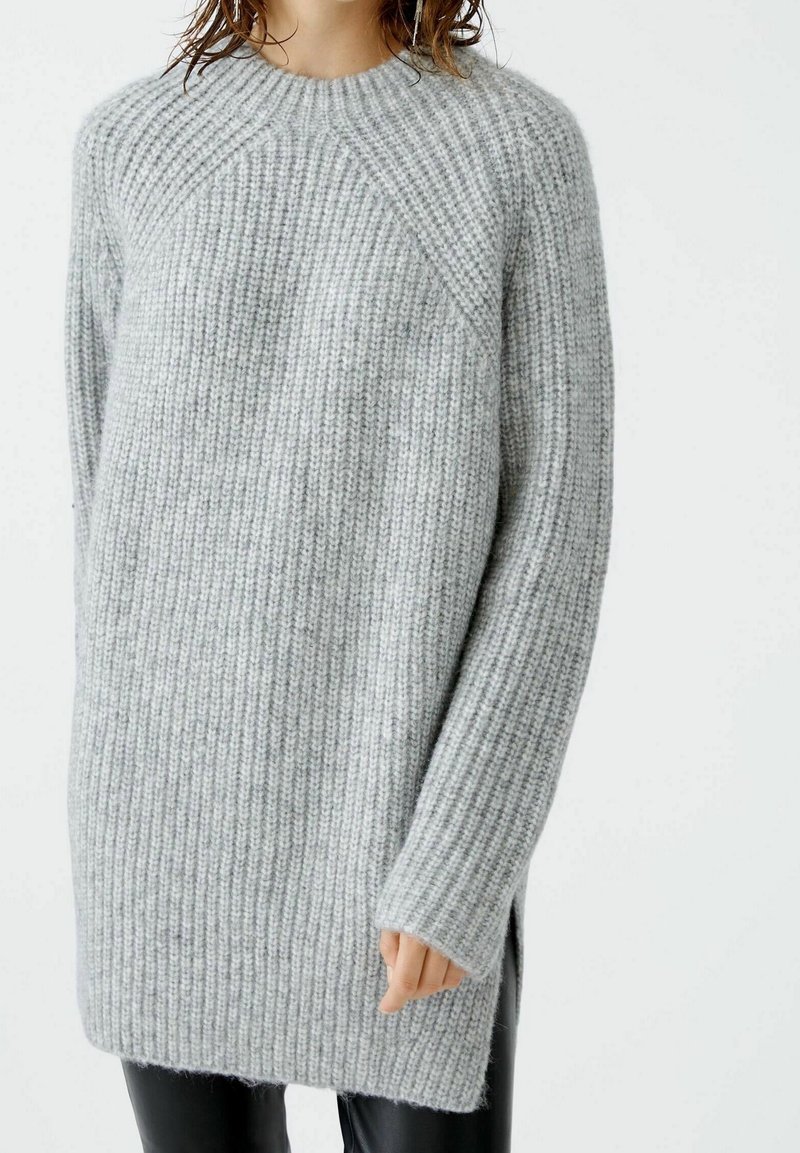 Pull en tricot gris avec texture côtelée, col rond, manches longues, fentes sur les côtés et coupe décontractée, fabriqué en mélange de laine douce.