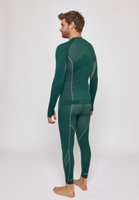 Un haut à manches longues vert et des leggings ajustés en tissu texturé, avec des coutures blanches contrastantes et un motif géométrique dans le dos.