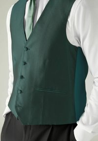 Green patterned vest with a textured finish, featuring six buttons, a side pocket, and a satin tie, worn over a white shirt.