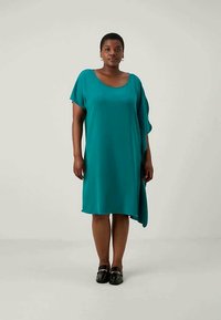 Teal, knee-length dress with a relaxed fit and asymmetrical hem. Short sleeves and a round neckline, made of smooth fabric.