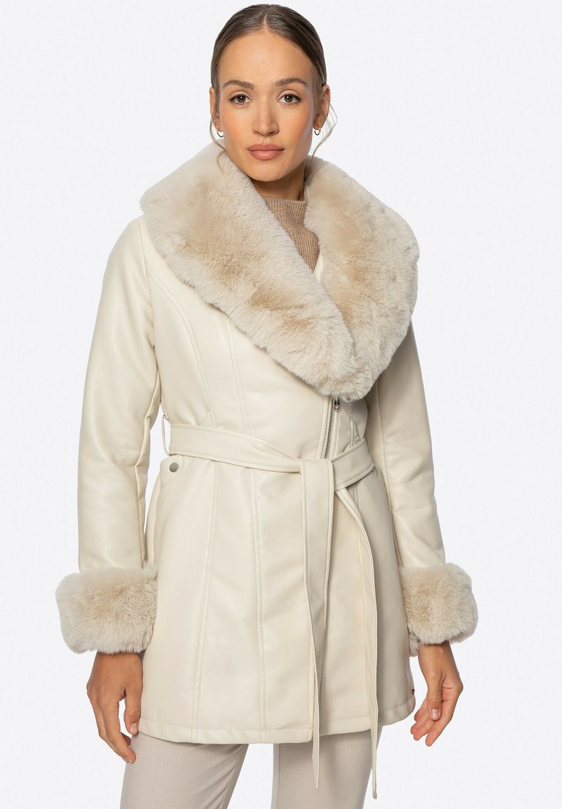 Kremowy skórzany płaszcz z szerokim futrzanym kołnierzem i akcentami na mankietach. Posiada paskowany talia, zamek błyskawiczny oraz pionowe szwy dla lepszej struktury.