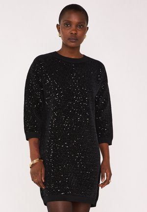 Abito nero con paillettes, maniche tre quarti, scollo a giro e polsini a coste. Tessuto liscio con superficie lucida, taglio fino al ginocchio.