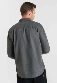 Camisa de manga larga gris con un diseño de yugo trasero, con un cuello tipo collarete y una textura suave, combinada con pantalones negros.
