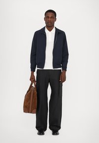 Marine bomberjakke, hvit polo skjorte, svarte vide bukser, brun semsket skinn weekendbag, båret med svarte sko. Enkel, moderne design.