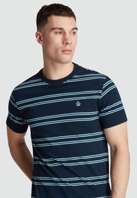 Navy blue cotton T-shirt with horizontal light blue stripes, short sleeves, and a small embroidered logo on the left chest.