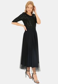 Czarny top z cekinami i rękawami do trzy czwarte, połączony z zwiewną czarną spódnicą z tiulu. Srebrne sandały na wysokim obcasie z ozdobami.