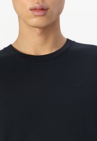 Tamno plava pamučna majica s okruglim izrezom i kratkim rukavima, koja sadrži diskretan logo izvezen tamnom niti na prsima.