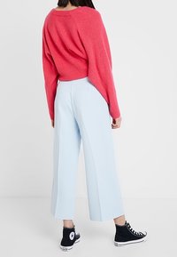 Pull en tricot rouge, pantalon large bleu clair, baskets montantes noires. Le pull a une coupe ample ; le pantalon a une texture douce.