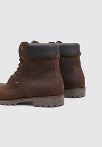 Bottes chelsea en cuir marron avec un col rembourré noir, œillets en métal et semelle en caoutchouc texturé. Présente un logo en relief sur le côté.