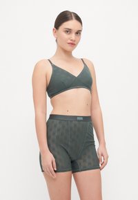 Bralette sans coutures de couleur vert foncé et short assorti, avec un motif texturé, des bretelles ajustables et une taille élastique douce.