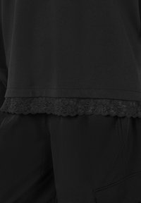 Top nero con orlo in pizzo, in cotone, vestibilità rilassata, abbinato a pantaloni neri in tessuto, texture liscia.