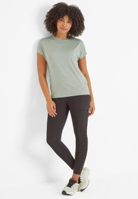 Light green short-sleeve shirt paired with black leggings, featuring a side pocket, and light green athletic shoes with black detailing.
