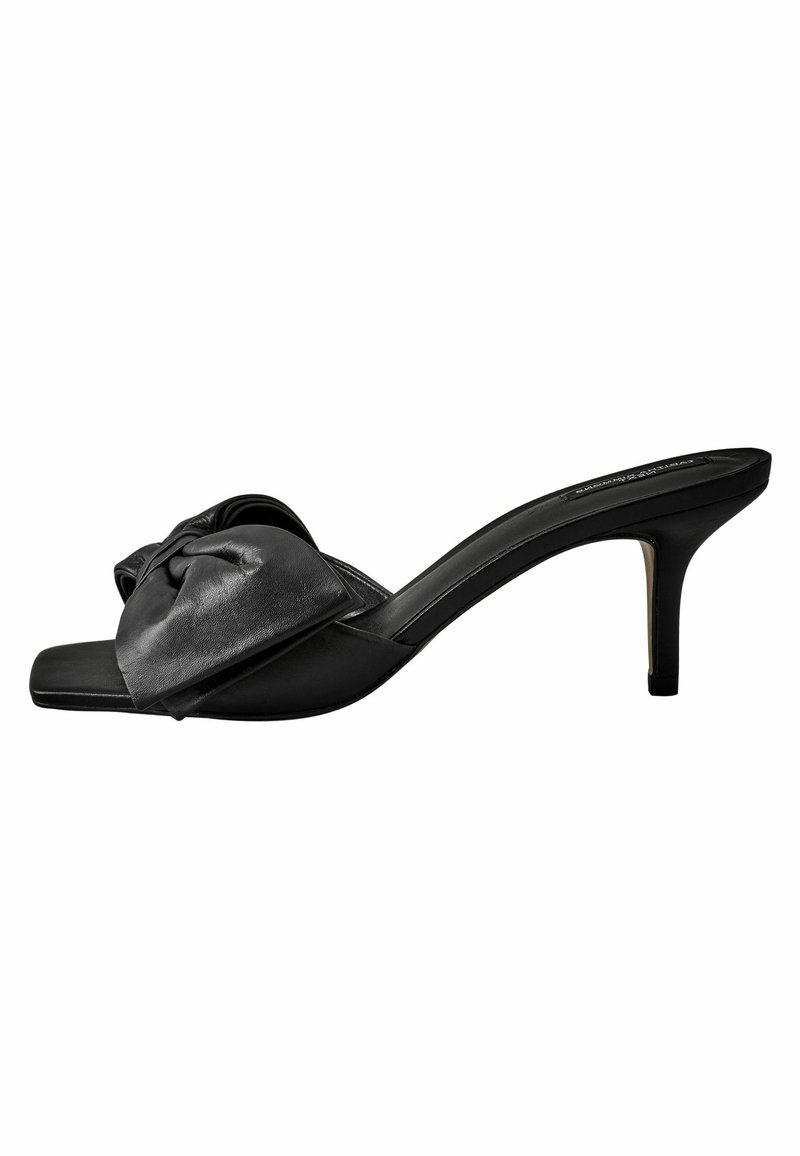 Sandale à talons en cuir noir avec un accent en nœud sur la large bride, design à bout ouvert et un talon stiletto élancé. Texture lisse dans l'ensemble.