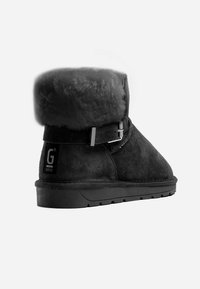 Botín negro de ante con un puño peludo, detalle de hebilla plateada y una suela de goma texturizada negra, ofreciendo un ajuste ceñido y calidez.