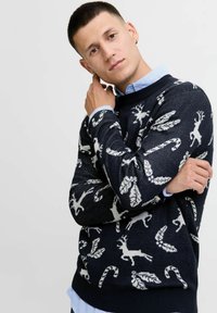 Pull en tricot bleu marine avec des motifs de rennes blancs, de cannes de Noël et de feuilles. Col et poignets côtelés, avec une finition texturée.