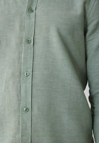 Close-up of a light green buttoned shirt front, focusing on fabric texture and evenly spaced round buttons.