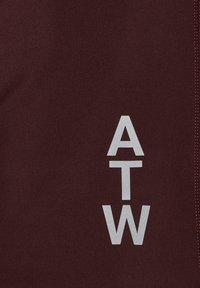 Burgundy tyg med en slät yta som har en vertikal vit "ATW"-logotyp och kontrasterande söm längs kanten.