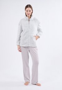 Szara, puszysta kurtka z polaru z wysokim kołnierzem i przednim zamkiem błyskawicznym. Do tego jasnoszare spodnie z czerwonym wzorem w kropki.