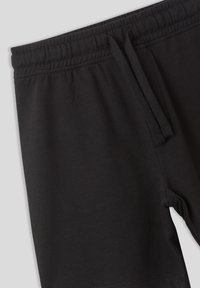 Pantaloni da tuta neri realizzati in tessuto morbido e flessibile, con una cintura elastica dotata di lacci e una silhouette affusolata.