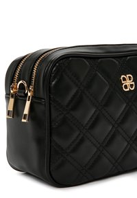 Bolso de cuero negro acolchado con herrajes dorados, que presenta doble cremallera y un panel frontal texturizado. Forma rectangular compacta.