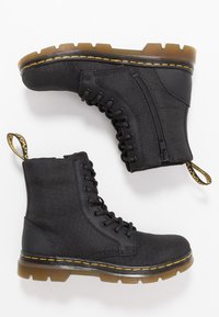 Black ankle boots made of durable fabric with a textured finish, featuring lace-up design, side zipper, and yellow stitching on a thick sole.