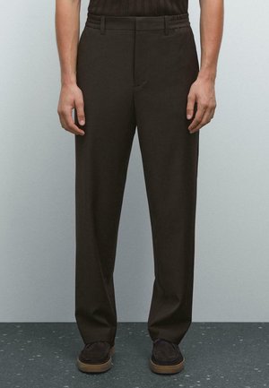 Pantalons marron à coupe décontractée, ceinture texturée, poches latérales et design à jambe droite, associés à des chaussures sombres.