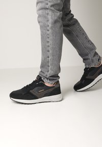 Sneaker nere e grigie con una tomaia in suede e mesh, dettagli testurizzati, una gomma intermedia bianca e una suola in gomma nera.