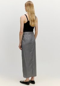 Grauer, langer Rock mit maßgeschneidertem Design, der eine glatte Textur und ein dezentes Muster aufweist. Getragen mit einem schwarzen Tanktop und flachen Schuhen.