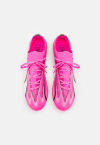 Scarpe da ginnastica di un vivace colore rosa con una parte superiore simile a una calza, caratterizzate da accenti neri e bianchi, pattern a strisce testurizzate e lacci tradizionali.