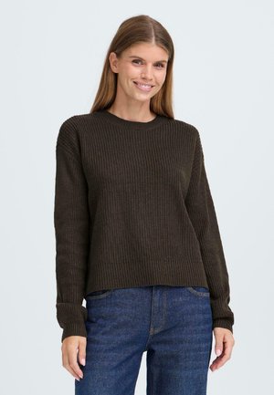 Mørkegrønn ribbet strikkegenser med lange ermer og rund hals, med en avslappet passform og teksturert mønster. Kombinert med blå jeans.