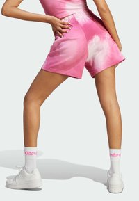 Shorts rosa tie-dye con vita elastica, tasche laterali e texture morbida. Indossati con sneakers bianche e calzini con accenti rosa.