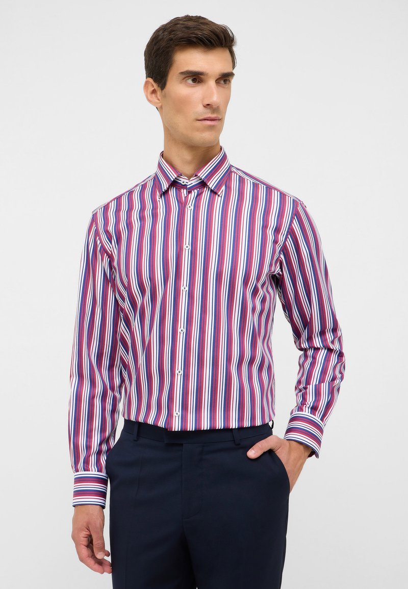 Camicia a maniche lunghe con bottoni e righe verticali in rosso, blu e bianco. Presenta un colletto classico e chiusura frontale con bottoni. Materiale in cotone.