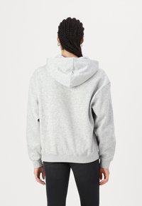 Gray, oversized hoodie with a soft texture, large hood, and ribbed cuffs and hem. Back view shows minimal detailing and no logos.