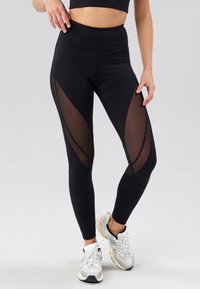 Leggings noirs avec panneaux en maille transparente sur les côtés, taille haute et coupe ajustée. Caractérisés par une texture lisse et une silhouette sportive.
