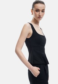 Top negro sin mangas con escote cuadrado, corsé ajustado y dobladillo peplum. Tejido suave con un diseño ceñido, combinado con pantalones negros.